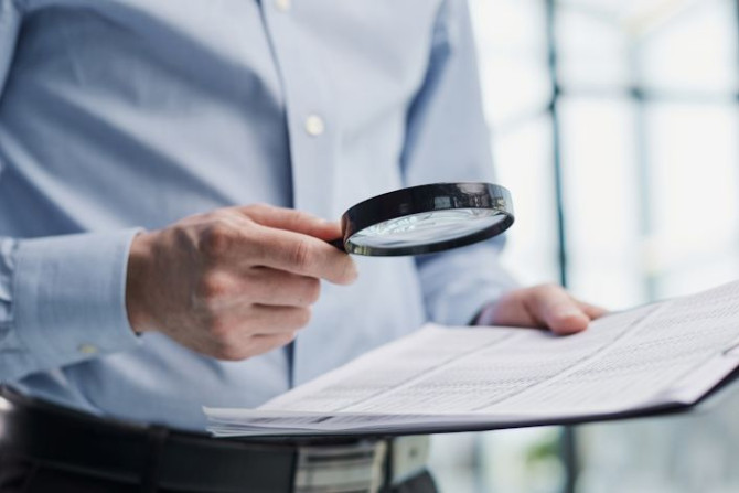 man-looking-through-magnifying-glass-documents-notebook.jpg